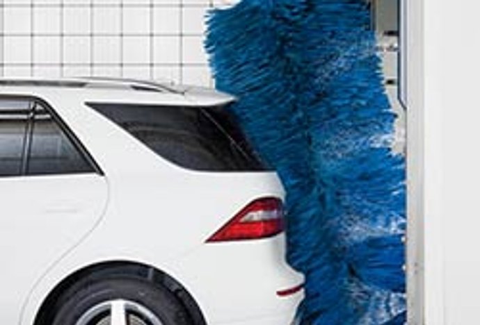Eine blaue Waschbürste reinigt einen weißen SUV in einer Waschstraße.